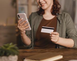 Smiley Woman Using Her Smartphone With Credit Card Home Scaled