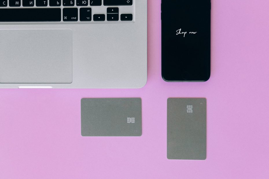 Laptop, cards, and smartphone on pink background for online shopping.